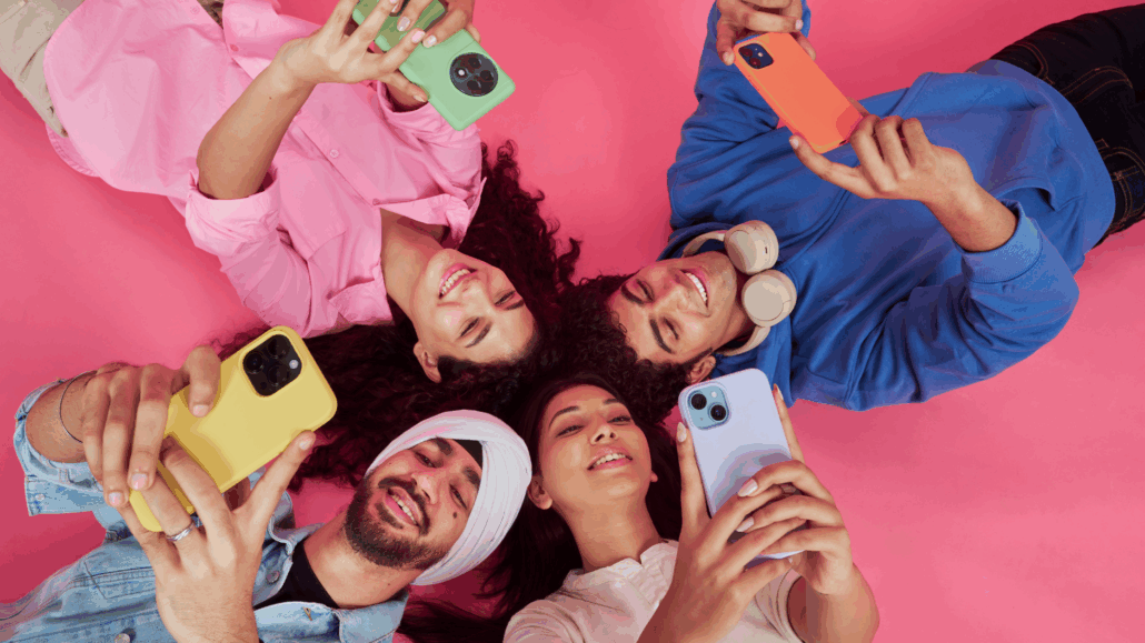 Quattro ragazzi sorridenti con smartphone in mano, su sfondo colorato e vivace. Simbolo dell'evoluzione del marketing generazionale.